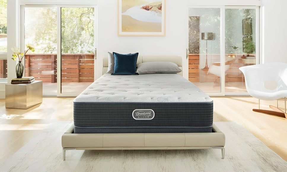 My Furniture modern queen mattress with gray and white quilted top, resting on a sleek beige upholstered platform bed frame in a bright, minimalist bedroom.
