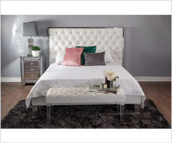 My Furniture white tufted upholstered bed with chrome trim, matching tufted bench with clear legs, styled with colorful pillows and mirrored nightstand on a dark shag rug.